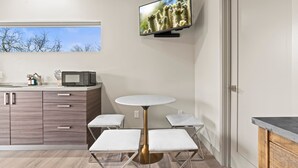 Une cuisine moderne avec une table ronde, des tabourets blancs rembourrés, un téléviseur à écran plat et un four à micro-ondes posé sur le plan de travail.