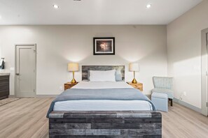 A bedroom with a bed, bedside lamps, a chair, a door, and a framed picture on the wall.