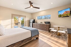 Une chambre avec un lit, un ventilateur de plafond, un coin cuisine et un téléviseur fixé au mur.