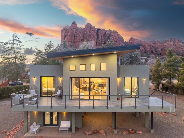A modern two-story house with a balcony, large windows, and a view of red rock formations.