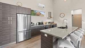 A modern kitchen with a stainless steel refrigerator, a built-in oven, and a large island with bar stools. - Moondance Red Rock Retreat | Views |Private Studio (Sedona)