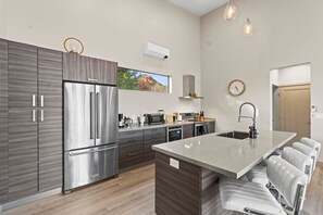 A modern kitchen with a stainless steel refrigerator, a built-in oven, and a large island with bar stools.