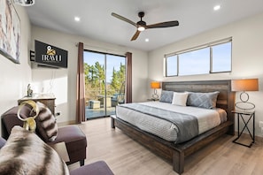 A modern hotel room with a large bed, a ceiling fan, a TV, and a view of the outdoors.