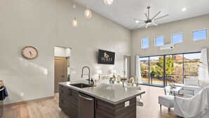 A modern kitchen with a large island, a dining area with a white sofa, and a view of red rock formations through large windows. - Moondance Red Rock Retreat | Views |Private Studio (Sedona)