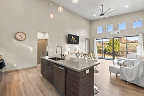 A modern kitchen with a large island, a dining area with a white sofa, and a view of red rock formations through large windows.