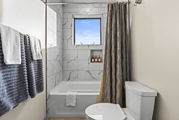 A bathroom with a bathtub, toilet, and a window above the bathtub.