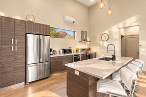A modern kitchen with a stainless steel refrigerator, a microwave, and a sink with a faucet. There is a window with a view of a mountain landscape.