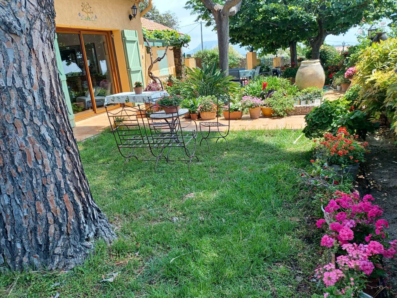 Un jardín con una mesa y sillas de metal, rodeado de plantas y flores en macetas.