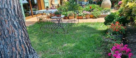 Un jardín con una mesa y sillas de metal, rodeado de plantas y flores en macetas.