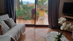 Ein Zimmer mit einer Couch, einem Fernseher und Blick auf einen Garten durch eine Schiebetür.