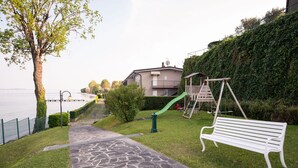 A park with a playground, a bench, a pathway, and a building in the background. - Specchio sul Lago (Manerba del Garda)