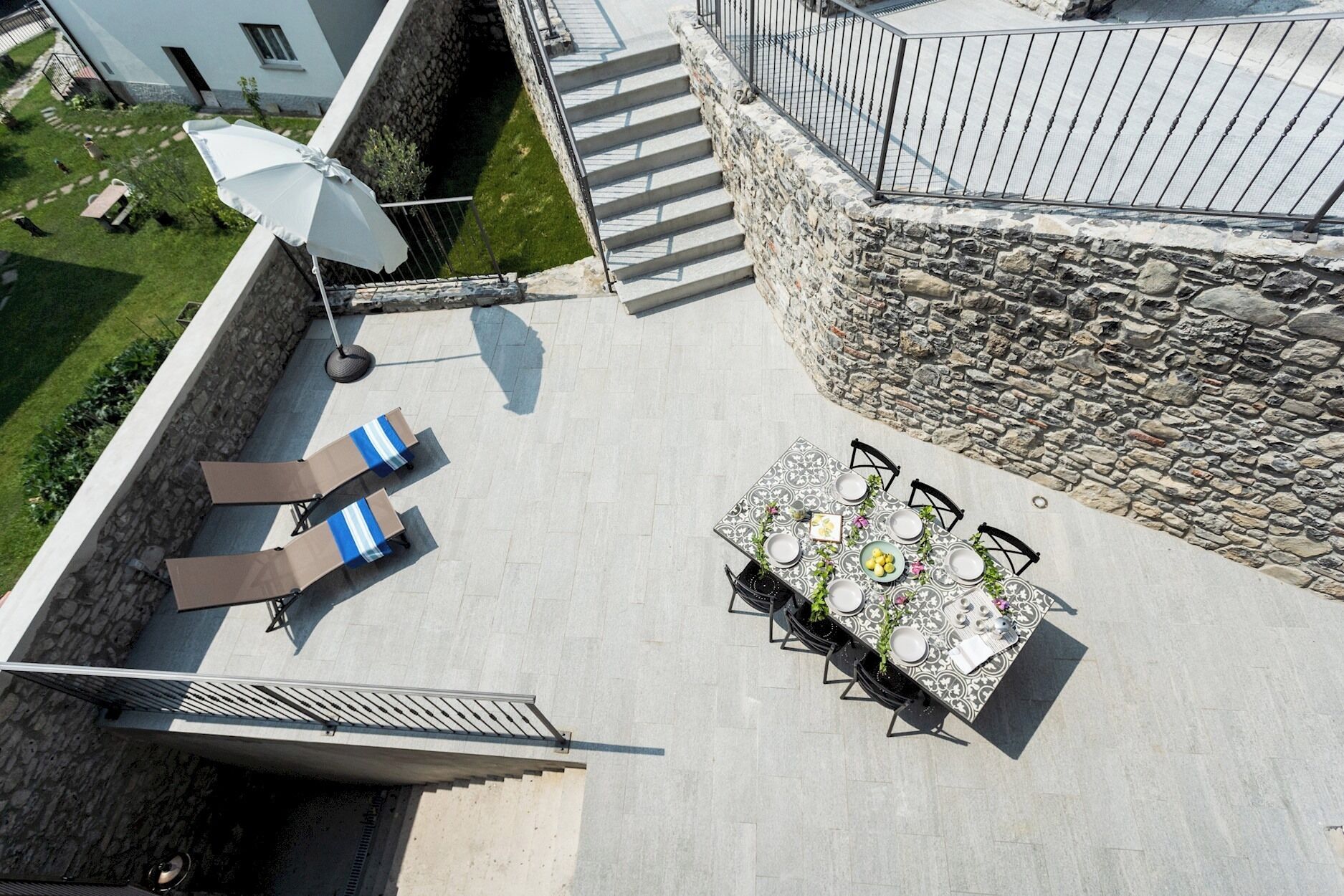 Une terrasse extérieure avec une table dressée pour les repas, un parasol et des chaises longues.