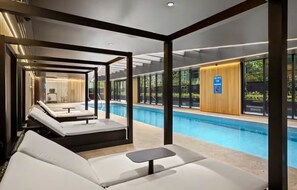 Ein moderner Poolbereich im Innenbereich mit Liegestühlen und einem kleinen Tisch, umgeben von Glaswänden und Holzverkleidung.