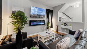 Ein modernes Wohnzimmer mit Flachbildfernseher, einer großen Pflanze, einem Sofa und einer Treppe.