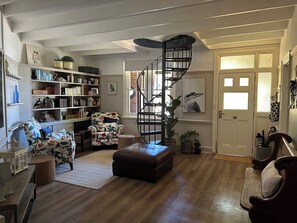 A cozy living room with a wooden floor, a floral armchair, a bookshelf, a spiral staircase, and a door with a window. - 3 bedroom home, Located on the main street of Crookwell (Crookwell)