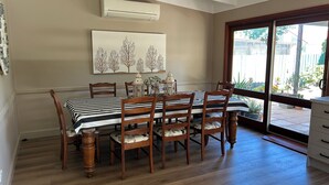 Een eethoek met een geruit tafelkleed, houten stoelen en een wandairconditioner.