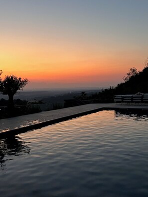 A serene sunset view over a calm pool with a tree silhouette and distant cityscape.