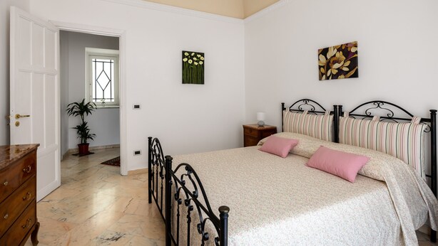 A bedroom with a bed, a dresser, a nightstand, a potted plant, and a window. - Torrekalsa Apartment by Wonderful Italy (Palermo)