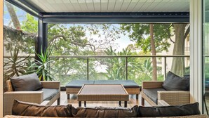 Un área de estar moderna al aire libre con mobiliario de mimbre y cojines, con vistas a un exuberante jardín y árboles.