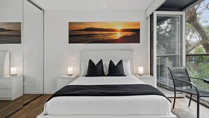 Un dormitorio moderno con una cama grande, vista al atardecer por la ventana y un balcón con una silla.