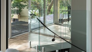 Un interior moderno con amplios ventanales, piso de madera y una escalera que conduce a un espacio exterior.