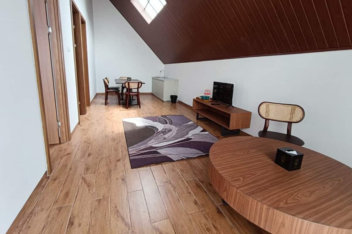 Un salon moderne avec un plancher en bois, un coin repas avec des chaises, un téléviseur posé sur un meuble en bois et une fenêtre laissant entrer la lumière naturelle.