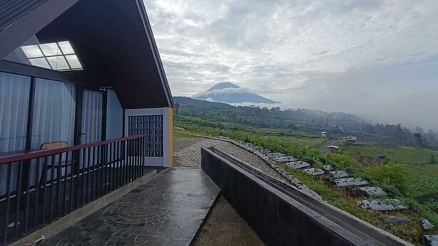 Un edificio moderno con techo inclinado y ventanas amplias, con vistas a un paisaje verde y una montaña.