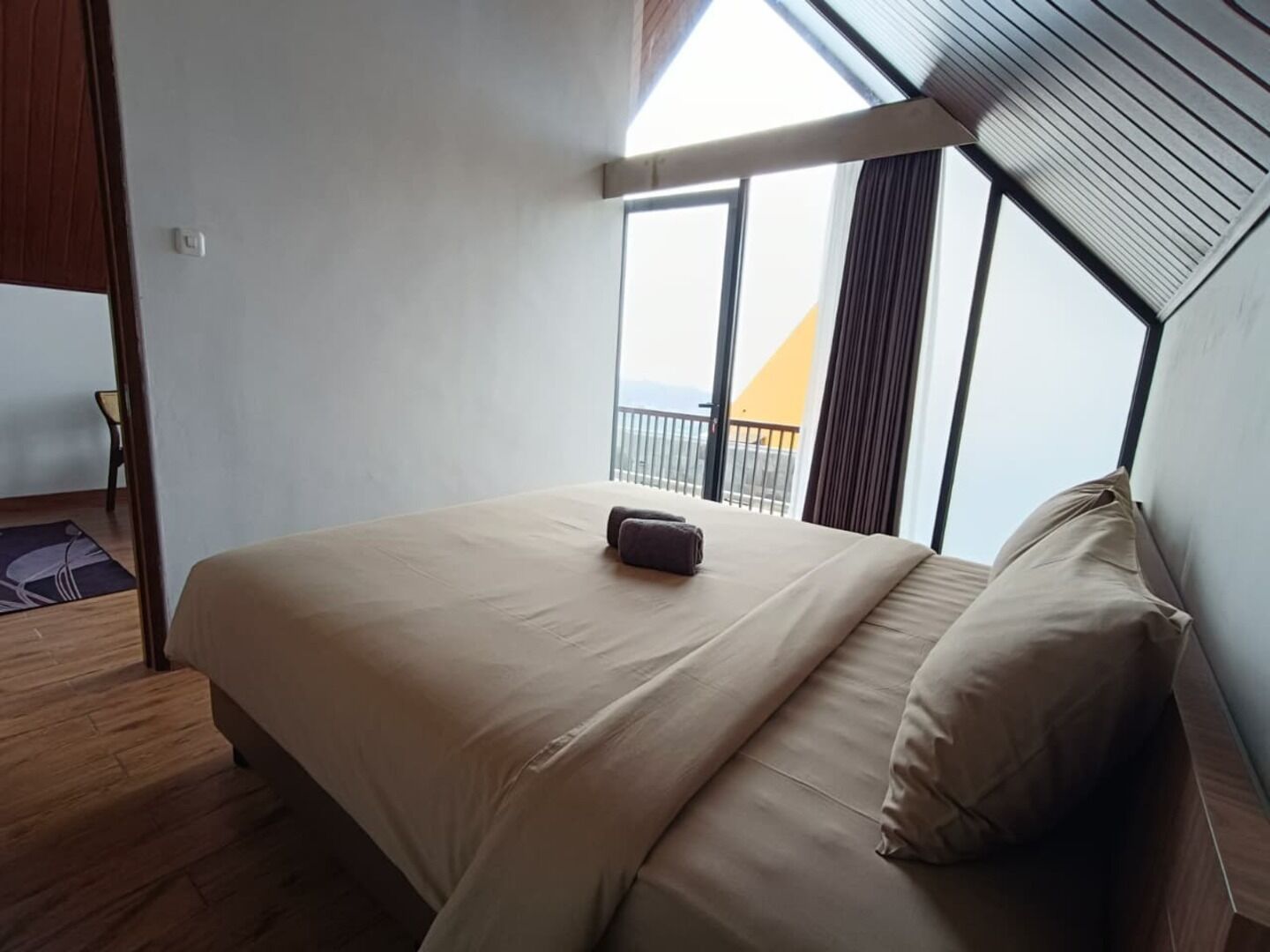 A bedroom with a large bed, a view of the outside, and a balcony.