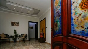 Eine Lobby mit gefliestem Boden, zwei Sofas, einem Blumentopf, einer Gitarre und einer Tür mit farbigem Glaspanel.