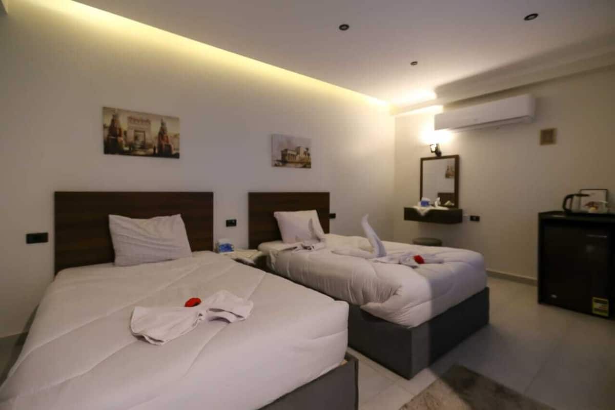 A hotel room with two beds, a desk, and a mirror.
