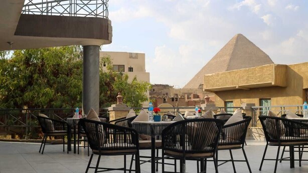 Ein Sitzbereich im Freien mit Tischen und Stühlen, im Hintergrund eine Pyramide und ein modernes Gebäude.