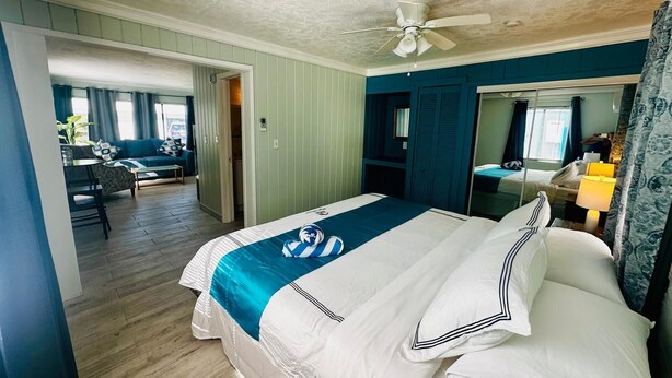 A hotel room with a bed, a ceiling fan, a bathroom mirror, and a view of the dining area. - Experience the passion of hospitality, cleaning, and good location! (Bradenton Beach)