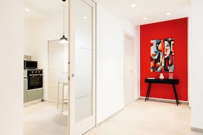 Une cuisine moderne dotée d’un four encastré, d’un coin repas aux couleurs claires et d’un mur d’accent rouge orné d’œuvres d’art abstraites.
