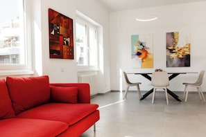 Un salon moderne avec un canapé rouge, une table à manger et des chaises, et des œuvres d’art abstraites accrochées aux murs.