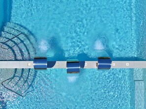Vista aérea de una piscina con tres tableros de salto y un bordeado de baldosas.