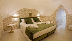 A bedroom with a stone wall, a bed with green bedding, and two bedside lamps. - Grotta Saracena (Porto Cesareo)
