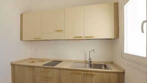 A compact kitchen with light wood cabinets, a stainless steel sink, and a window providing natural light. - Grotta Saracena (Porto Cesareo)