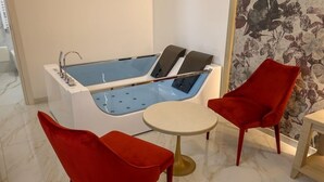 A modern bathroom with a bathtub, two red chairs, and a small round table. - Grotta Saracena (Porto Cesareo)