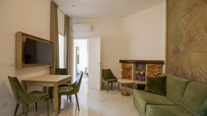 A modern living room with a dining area, a green sofa, and a TV mounted on the wall. - Grotta Saracena (Porto Cesareo)