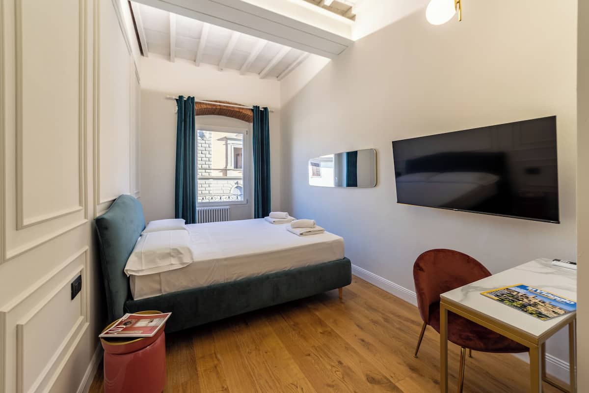 A modern hotel room with a bed, a TV, a desk, and a window with curtains.
