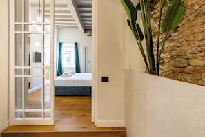 A hallway leading to a bedroom with a bed, a TV, and a stone wall. - Leovinci rooms (Florence)