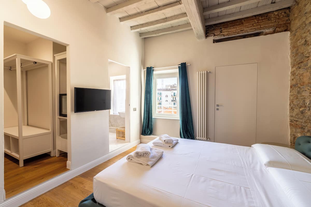 A bedroom with a large bed, a TV, a window with curtains, and a stone wall.