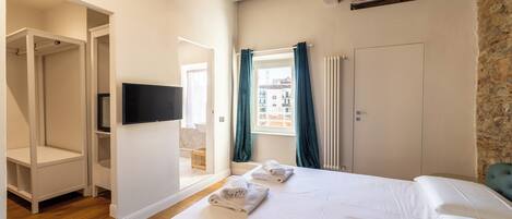 A bedroom with a large bed, a TV, a window with curtains, and a stone wall.