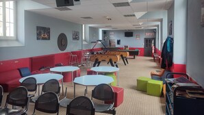 A room with tables and chairs, a dartboard, and a pool table.