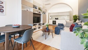Een moderne woonkamer met een eethoek, inbouwkasten, een flatscreen televisie en een gezellige zithoek met een bank en kussens.