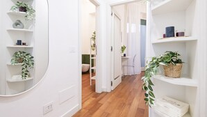 Een gang met witte muren, houten vloeren en planken met planten en boeken.
