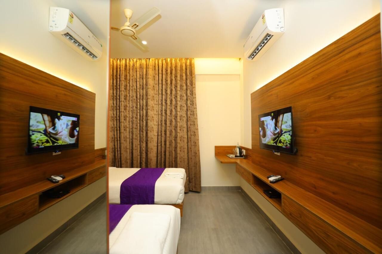 Habitación de hotel con dos camas, un televisor a cada lado, ventilador de techo y aire acondicionado.