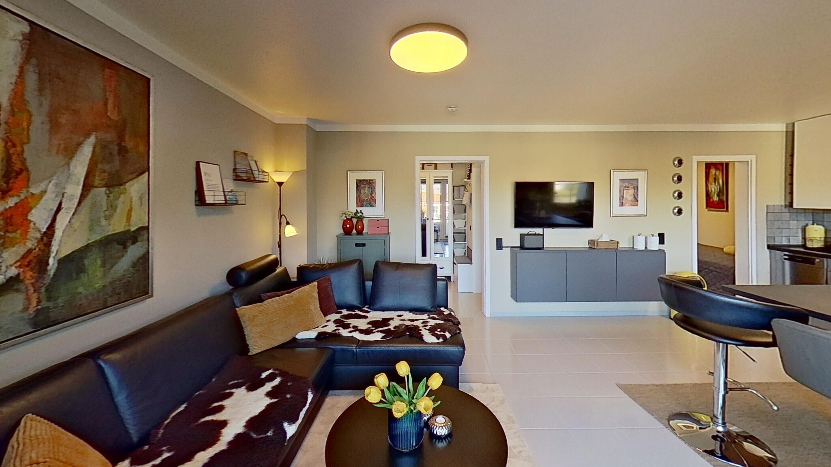 Een moderne woonkamer met een bank, salontafel en een televisie op de achtergrond.