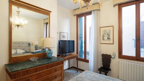 A hotel room with a large mirror, a television, a wooden dresser, a chair, and a window with a view. - Ca Lipoli (Venice)