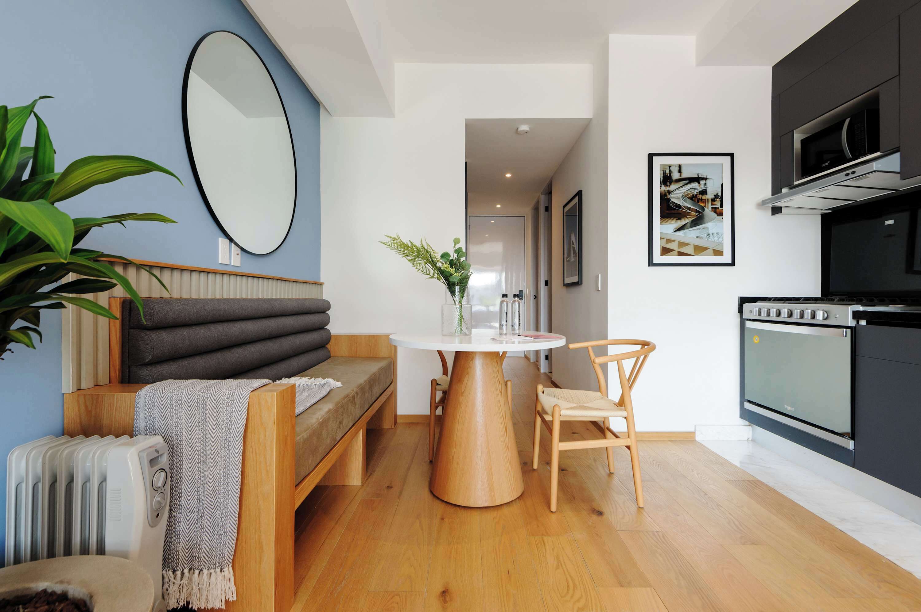 Eine moderne Küche mit Einbauofen und Mikrowelle, einem runden Holztisch mit Stühlen, einer Couch mit einer Sitzecke und einem großen Spiegel an der Wand.